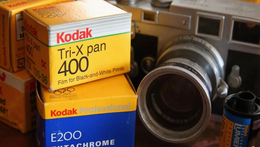 A film camera on a table beside boxes of Kodak black and white film
