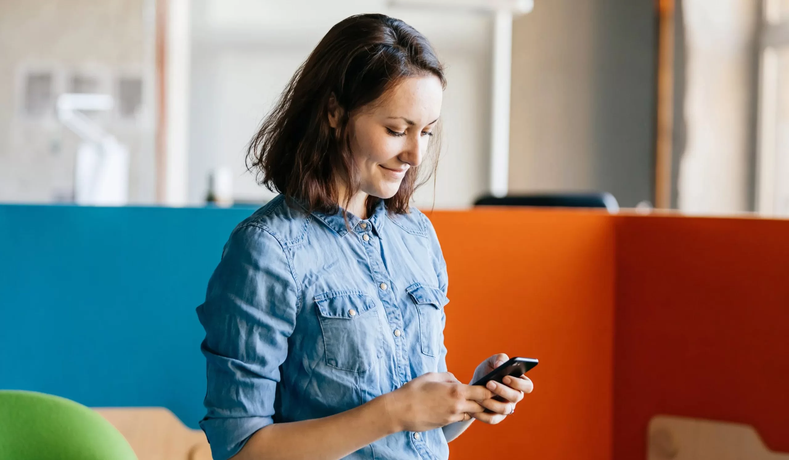 a young woman in a denim shirt is looking at her phone