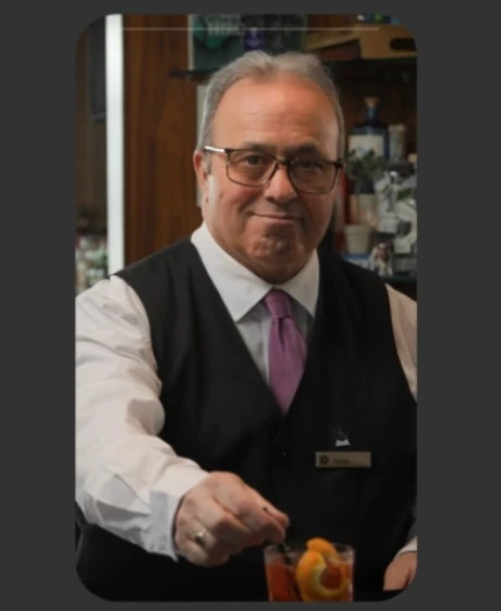 A bartender in a waistcoat stirs a cocktail in a bar